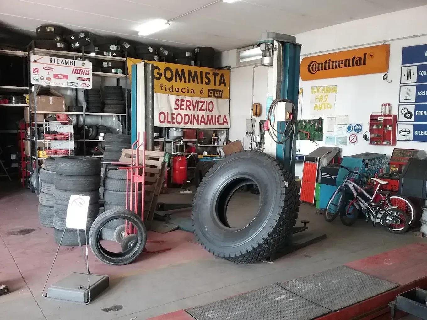 Interno di un'officina meccanica con pneumatici, attrezzi e una motocicletta rossa.