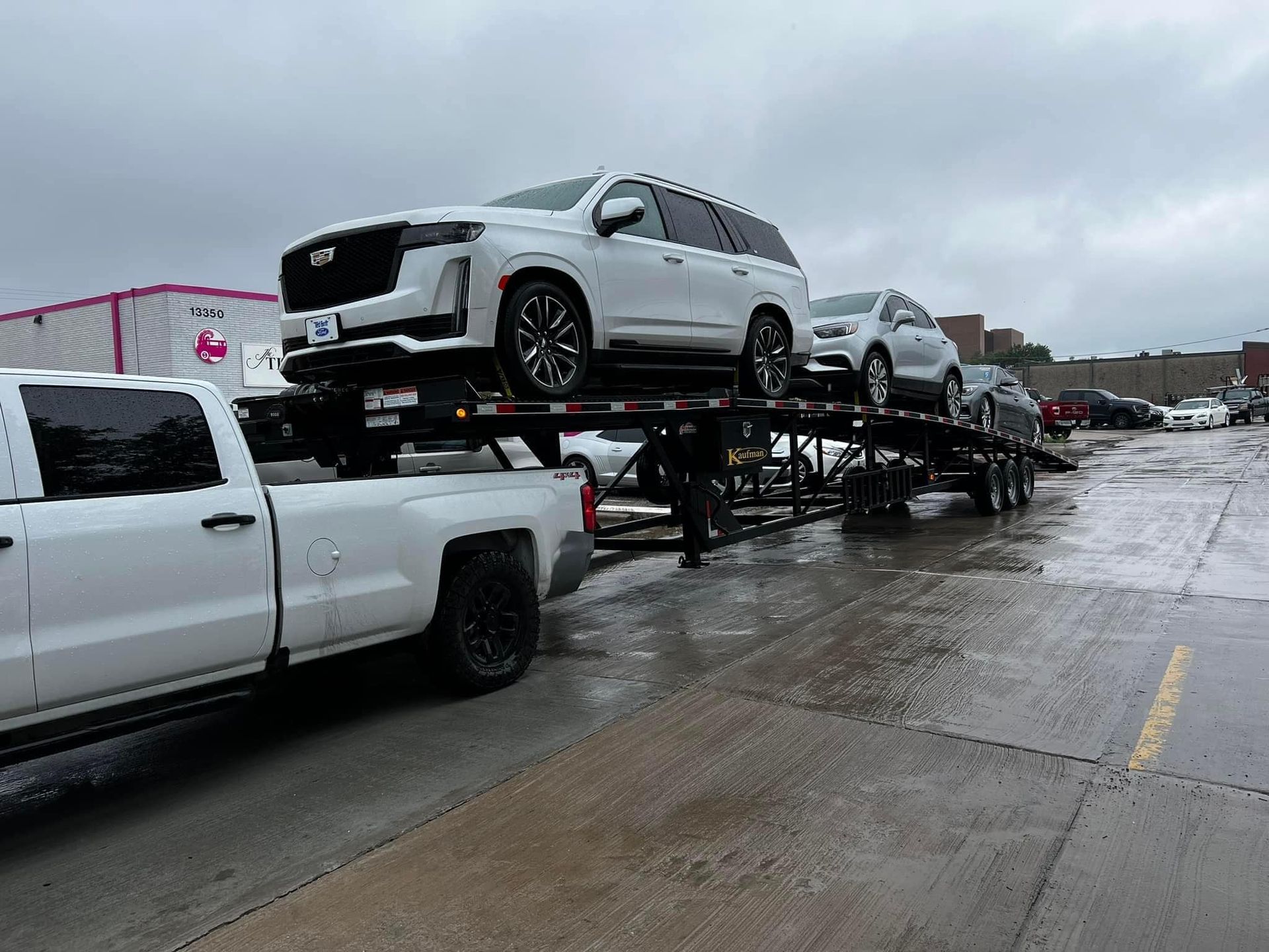 White truck hauling a trailer loaded with new white and silver SUVs on a wet, gray day.