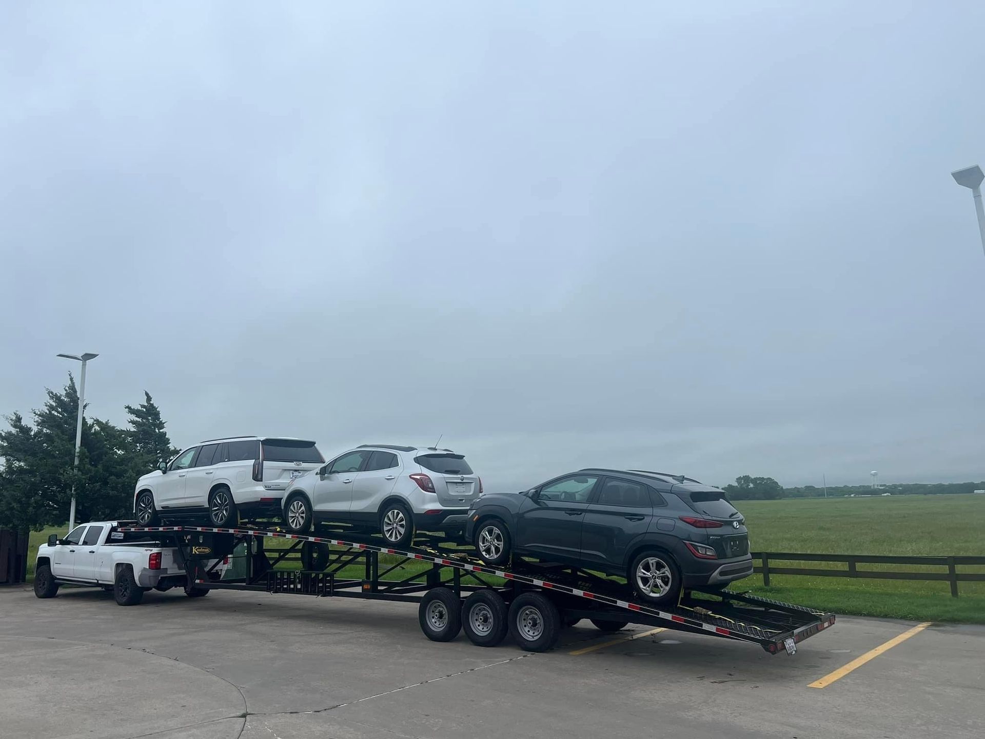 A car hauler loaded with four SUVs parked on a gray, overcast day.
