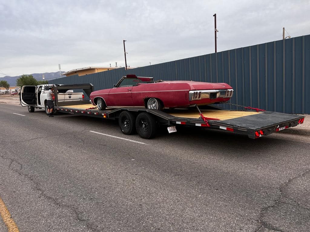 Red convertible car on a flatbed trailer, towed by a van, parked on a street.