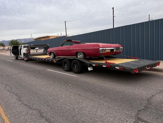 Red convertible car on a flatbed trailer, towed by a van, parked on a street.