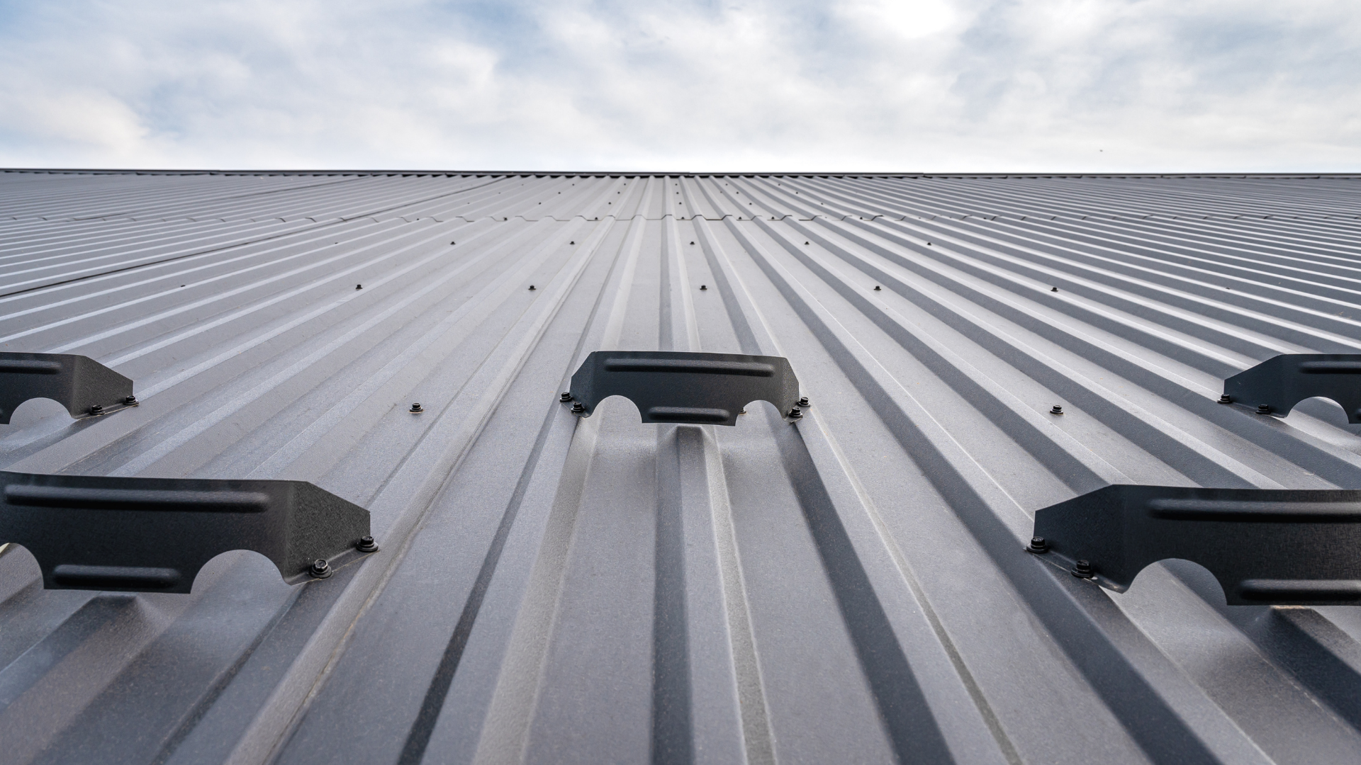 Corrugated metal roof with evenly spaced ridges and dark rooftop mounts under a bright sky