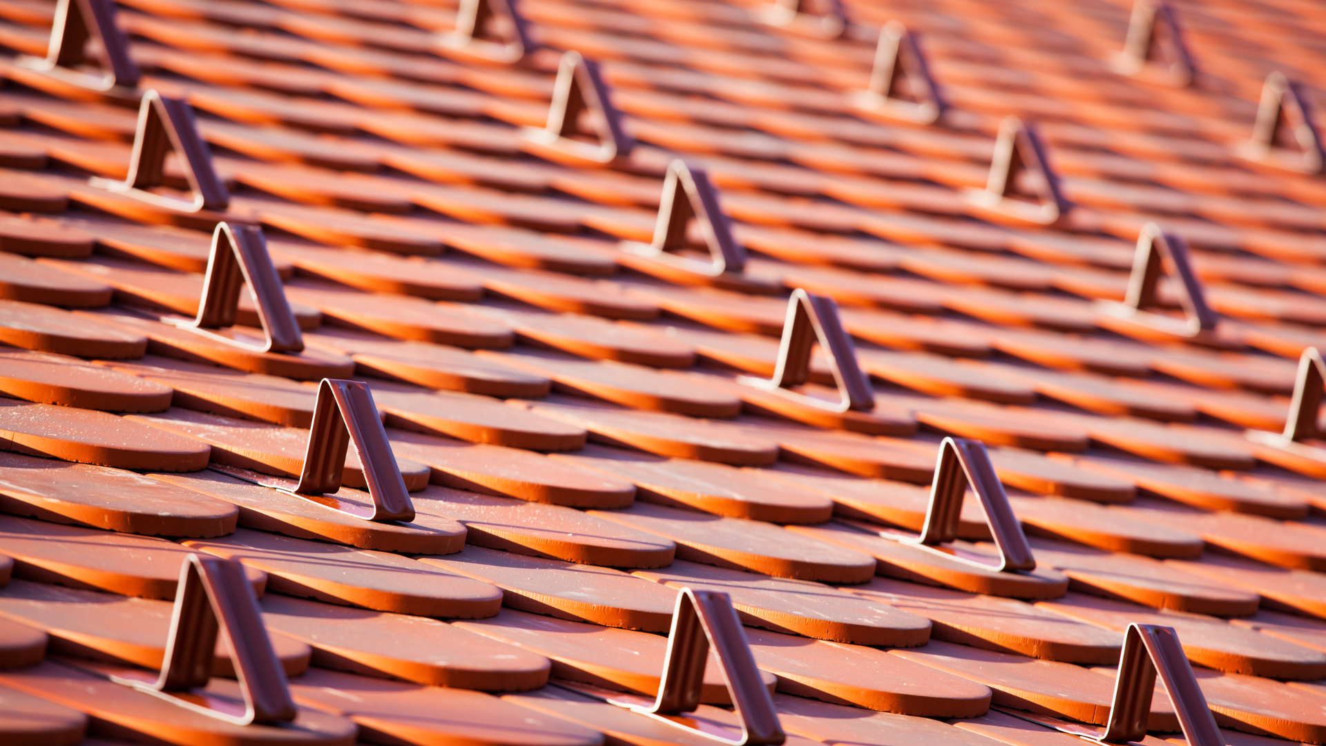 Rows of orange clay roof tiles with small metal brackets in a diagonal pattern