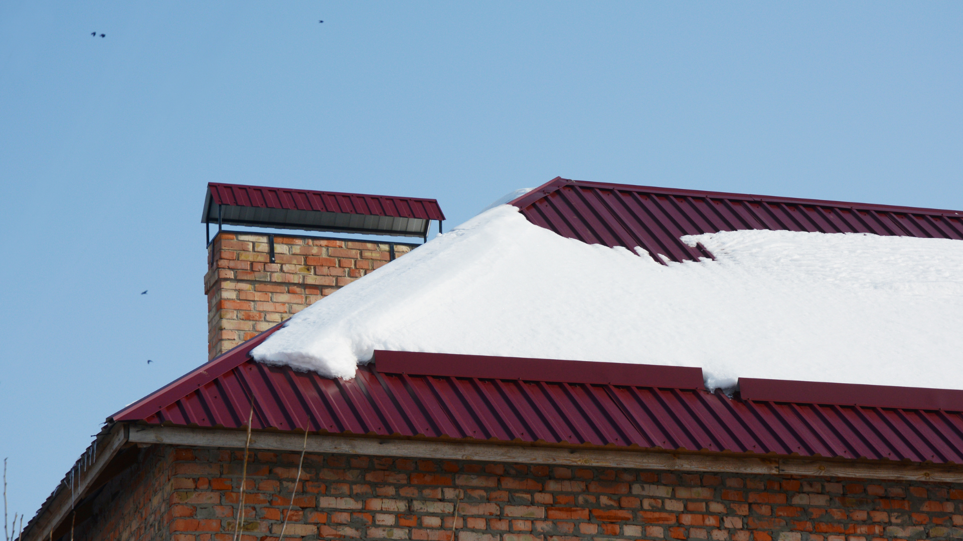 Snow-covered brick building with red metal roofs against a clear blue sky