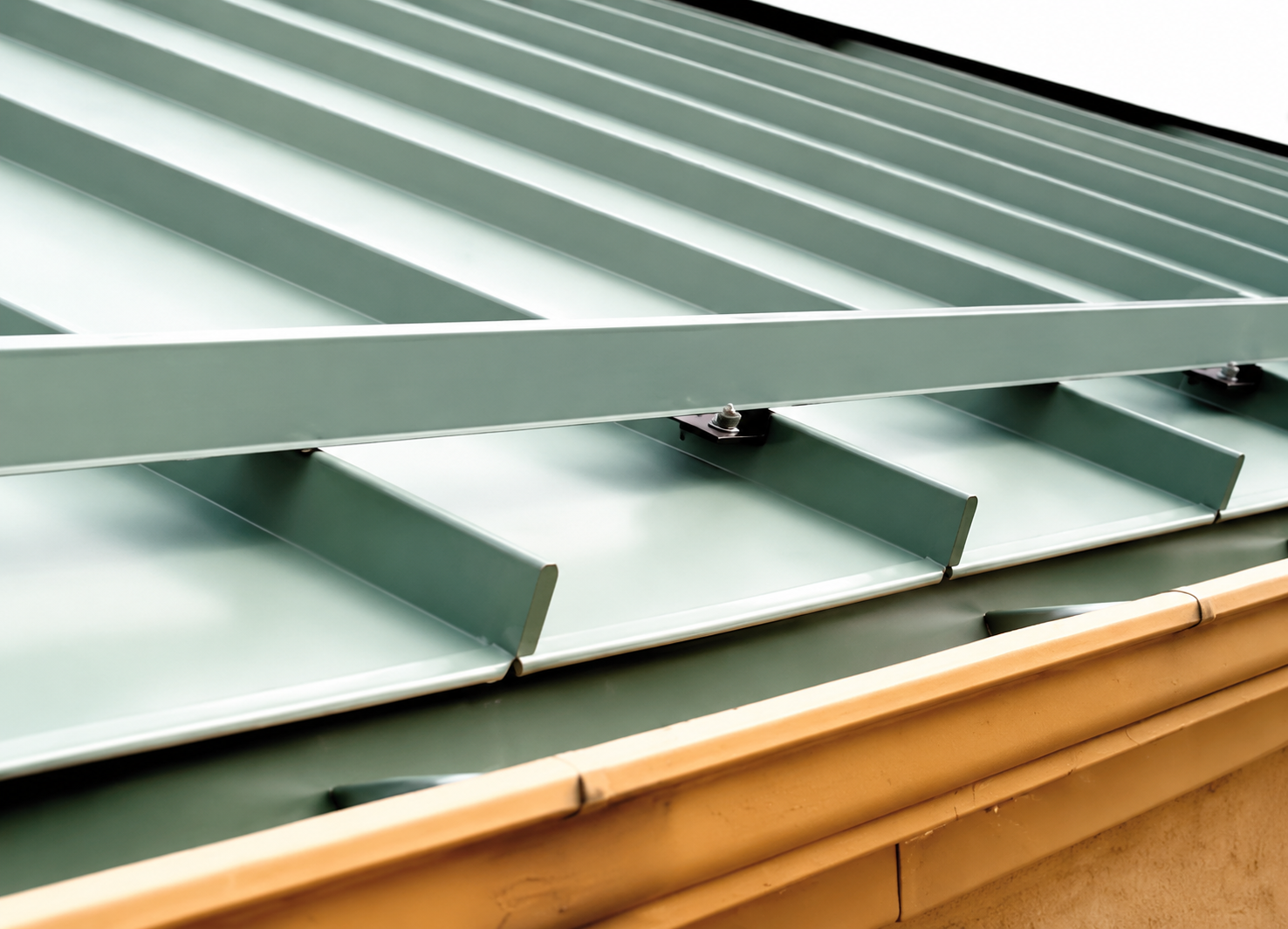 Green metal roof with raised seams and skylight vents above tan siding