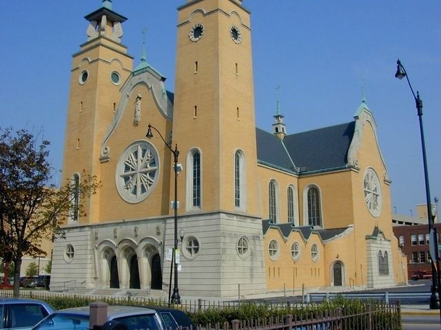 Yellow church with twin towers and a large circular rose window under a blue sky