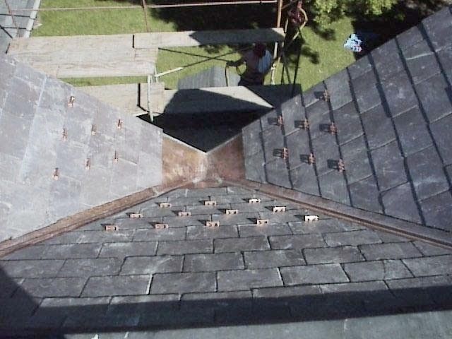Aerial view of a shingled roof with a central roof valley and small dormer, overlooking a yard below