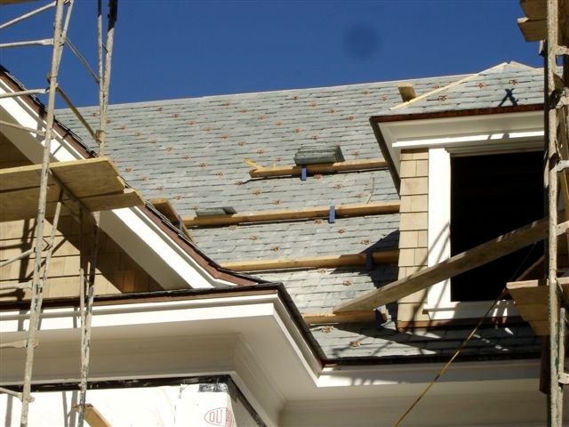 Roof under construction with scaffolding and exposed dormer windows beneath a blue sky