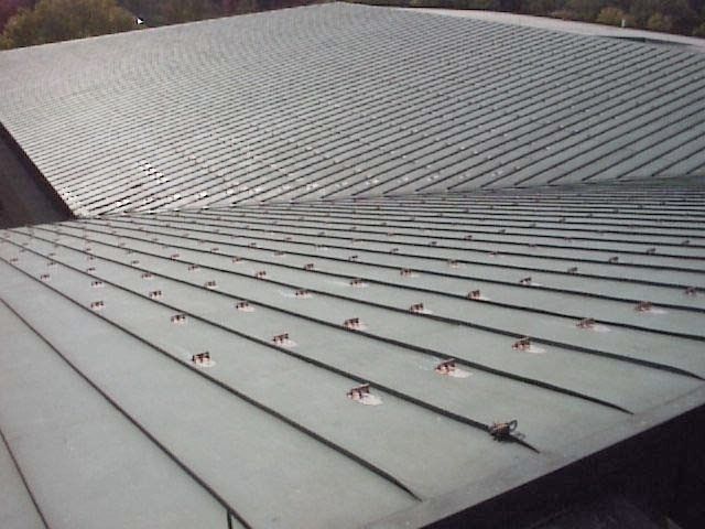 Curved gray metal roof with rows of small red fasteners or snow guards.