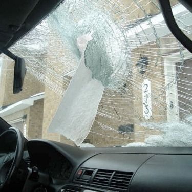 Cracked car windshield with a large hole and shattered glass, viewed from inside the vehicle.