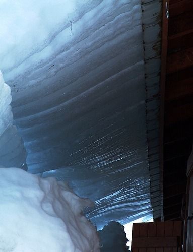 Large snowdrifts beside a corrugated metal roof overhang