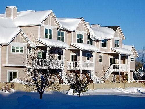 Snow-covered apartment buildings with balconies and trees under a clear blue sky