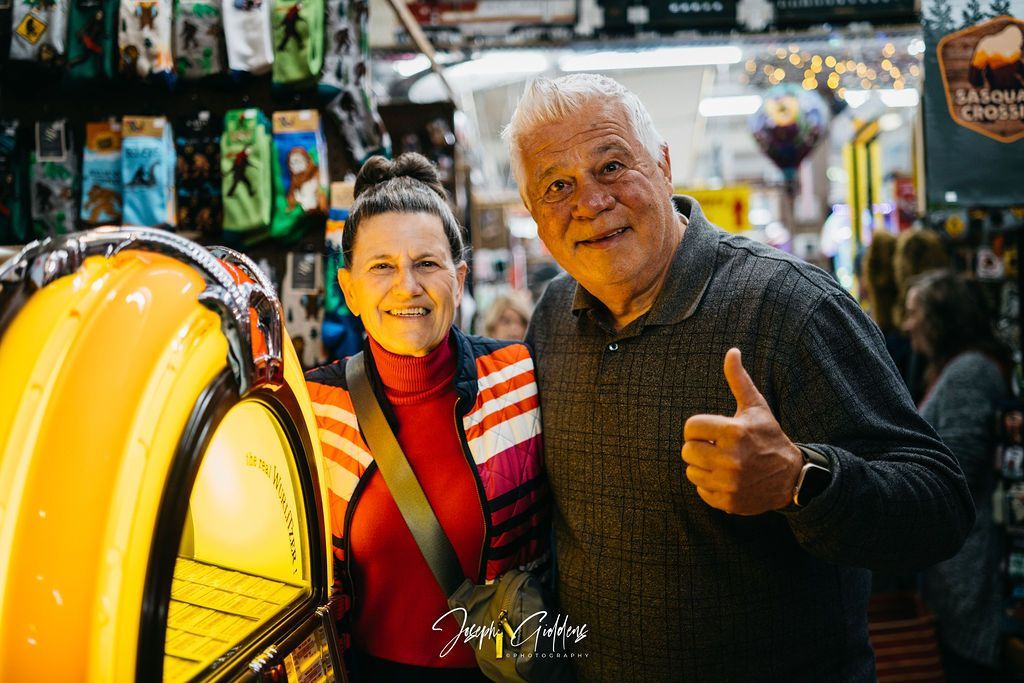 Two people pose next to a yellow jukebox in a store; the person on the right gives a thumbs up.