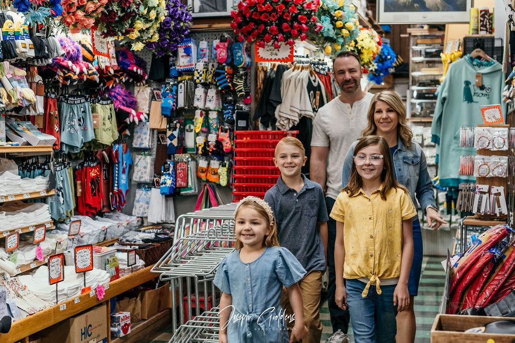 A family of four stands inside a crowded, colorful souvenir shop filled with hanging merchandise and shelves.