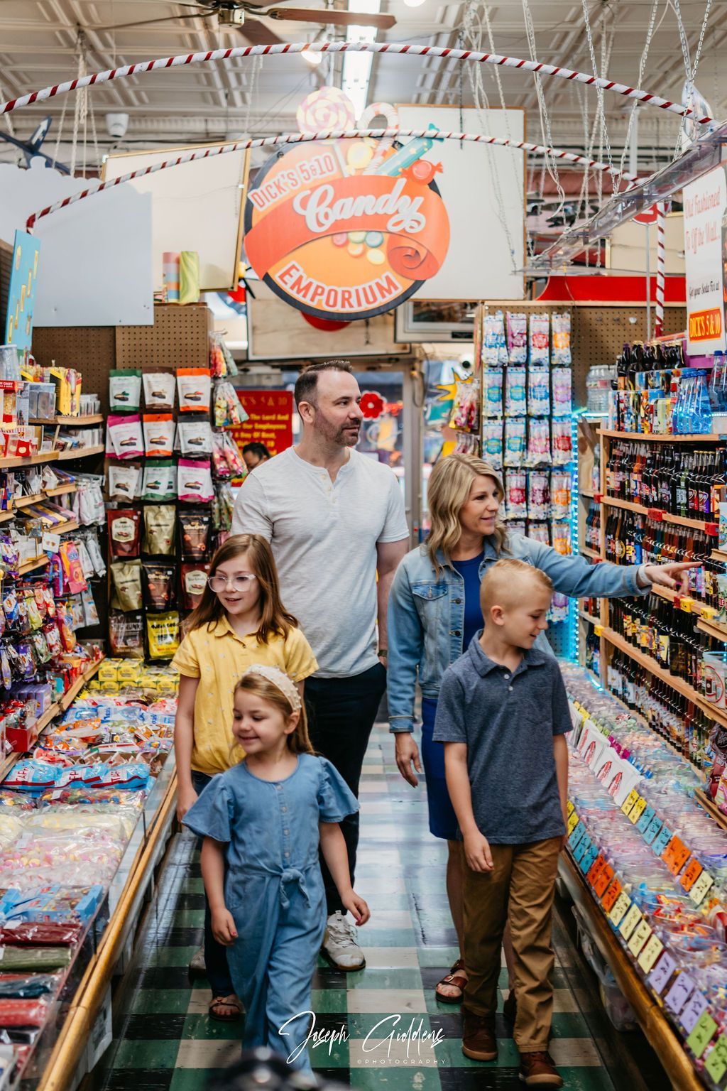 A family walks through a candy store aisle, smiling as they look at the shelves stocked with colorful sweets.