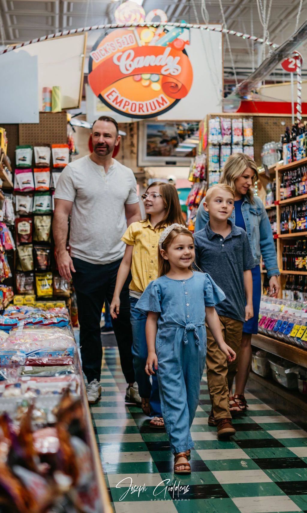 A family walks through a brightly lit candy shop with colorful displays and a checkered floor.