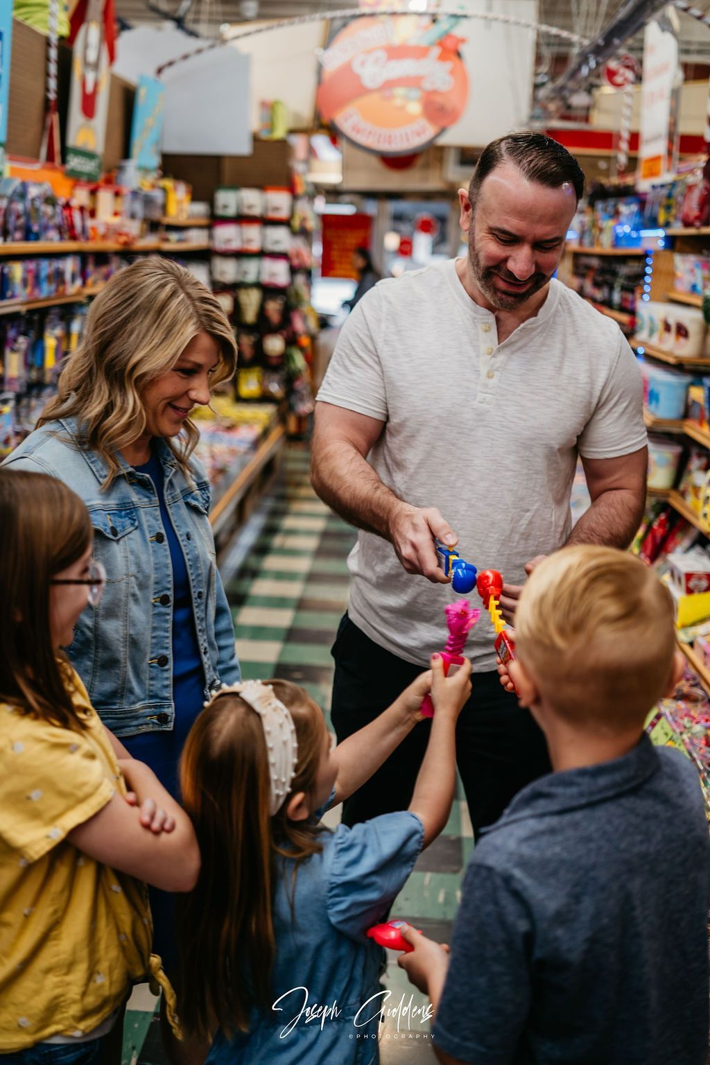 A family in a brightly lit, stocked grocery aisle shares playful bubble wands with one another.
