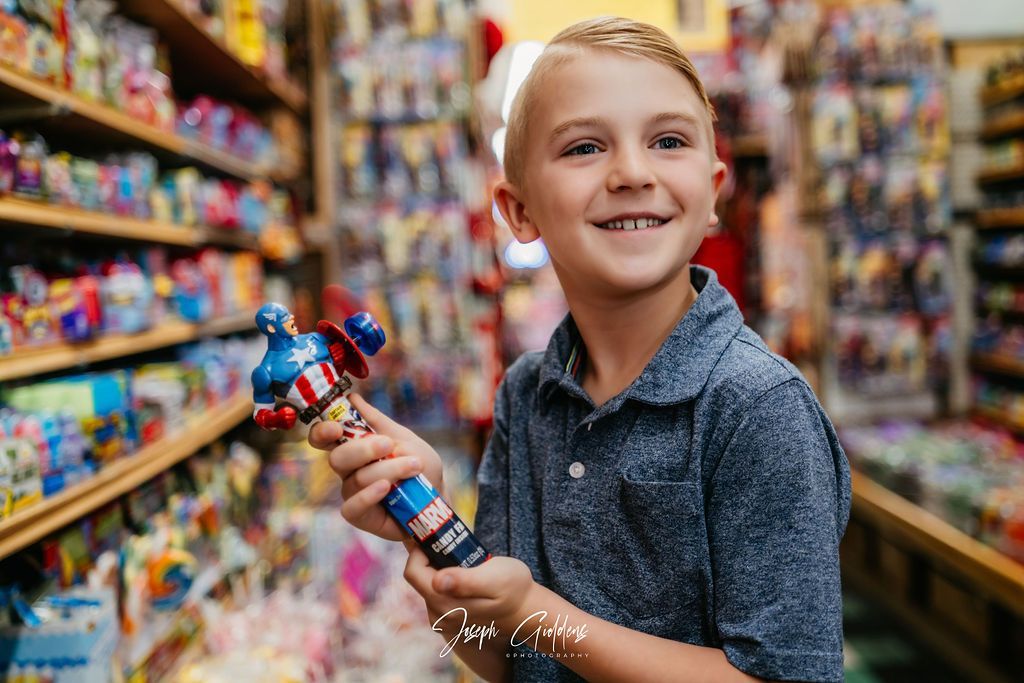 A smiling child in a blue polo shirt holds a Captain America action figure in a toy store aisle.