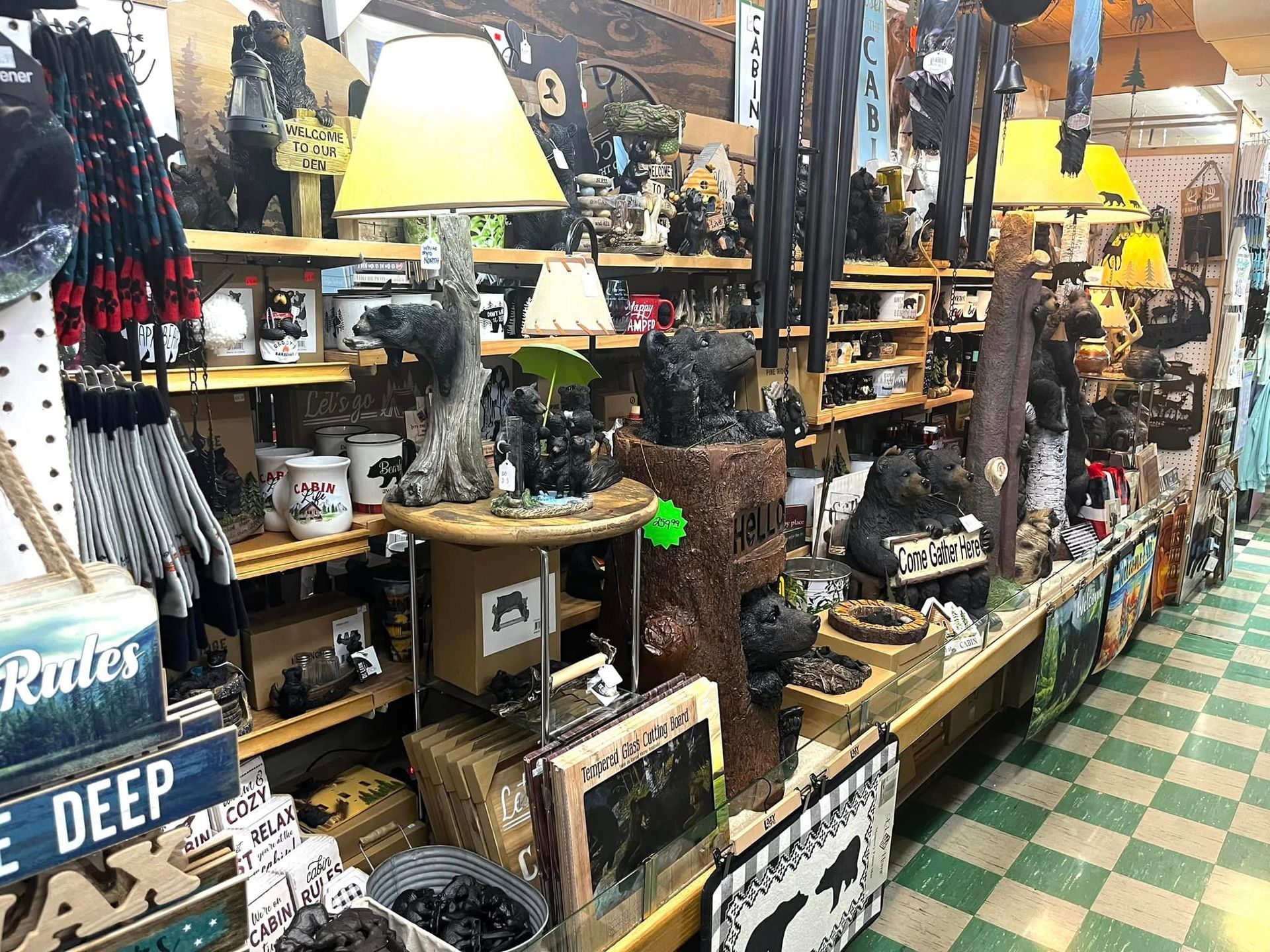 Retail shelf displaying rustic, bear-themed home decor including lamps, statues, and framed signs in a gift shop.