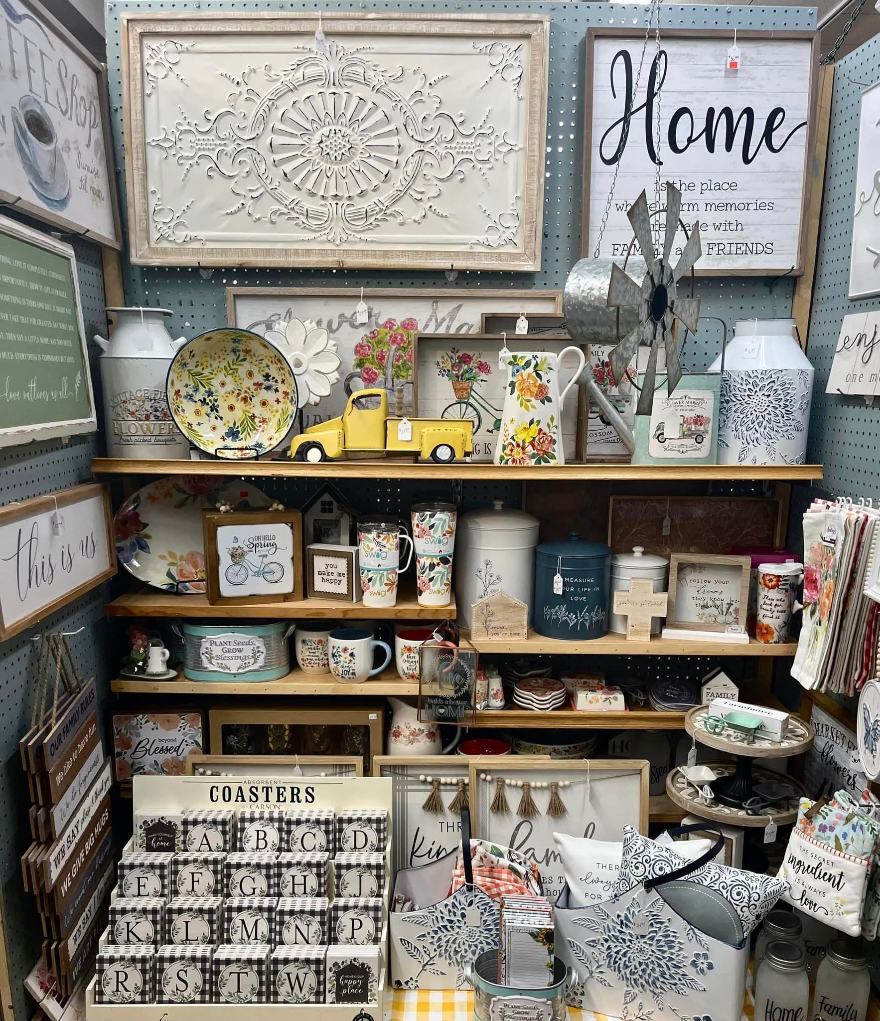 A store shelf display filled with decorative home decor, including metal signs, floral plates, and ceramic containers.