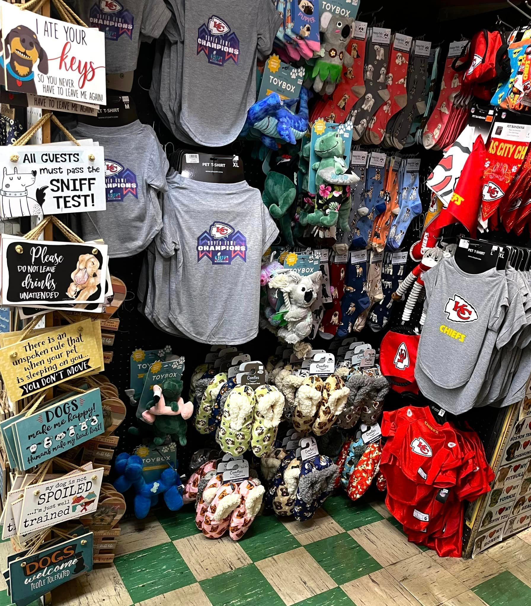 A retail display featuring grey pet t-shirts, patterned socks, and decorative signs with dog-themed text on a tiled floor.