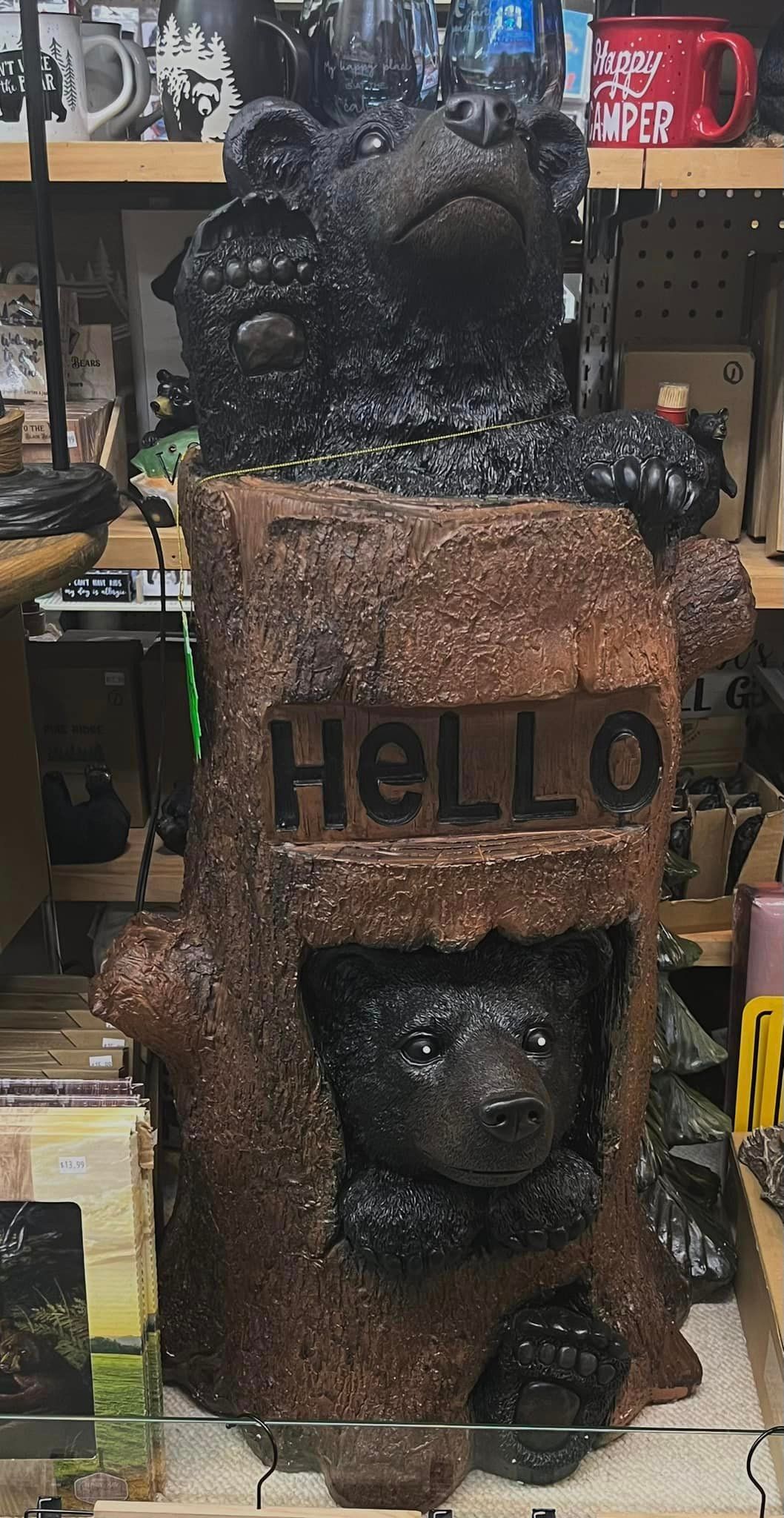 A brown decorative tree stump statue featuring a bear peeking out from a hole and another waving, with