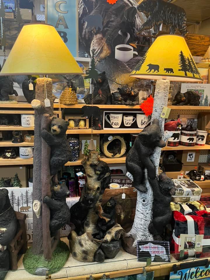 Two bear-themed floor lamps with yellow shades stand in a store, decorated with sculpted bears climbing tree trunks.
