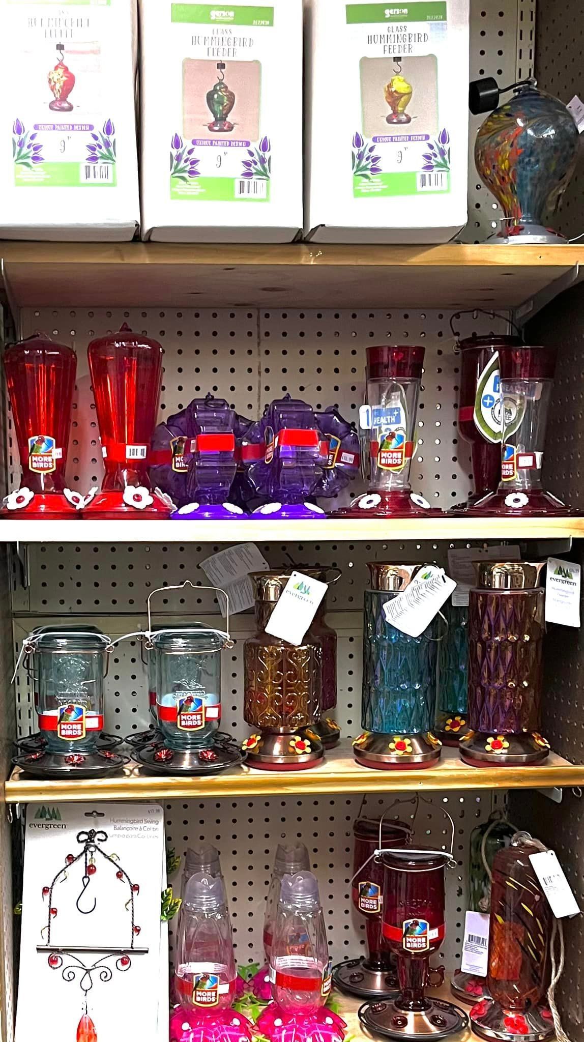 Store shelf display featuring various colorful glass hummingbird feeders and boxed products.