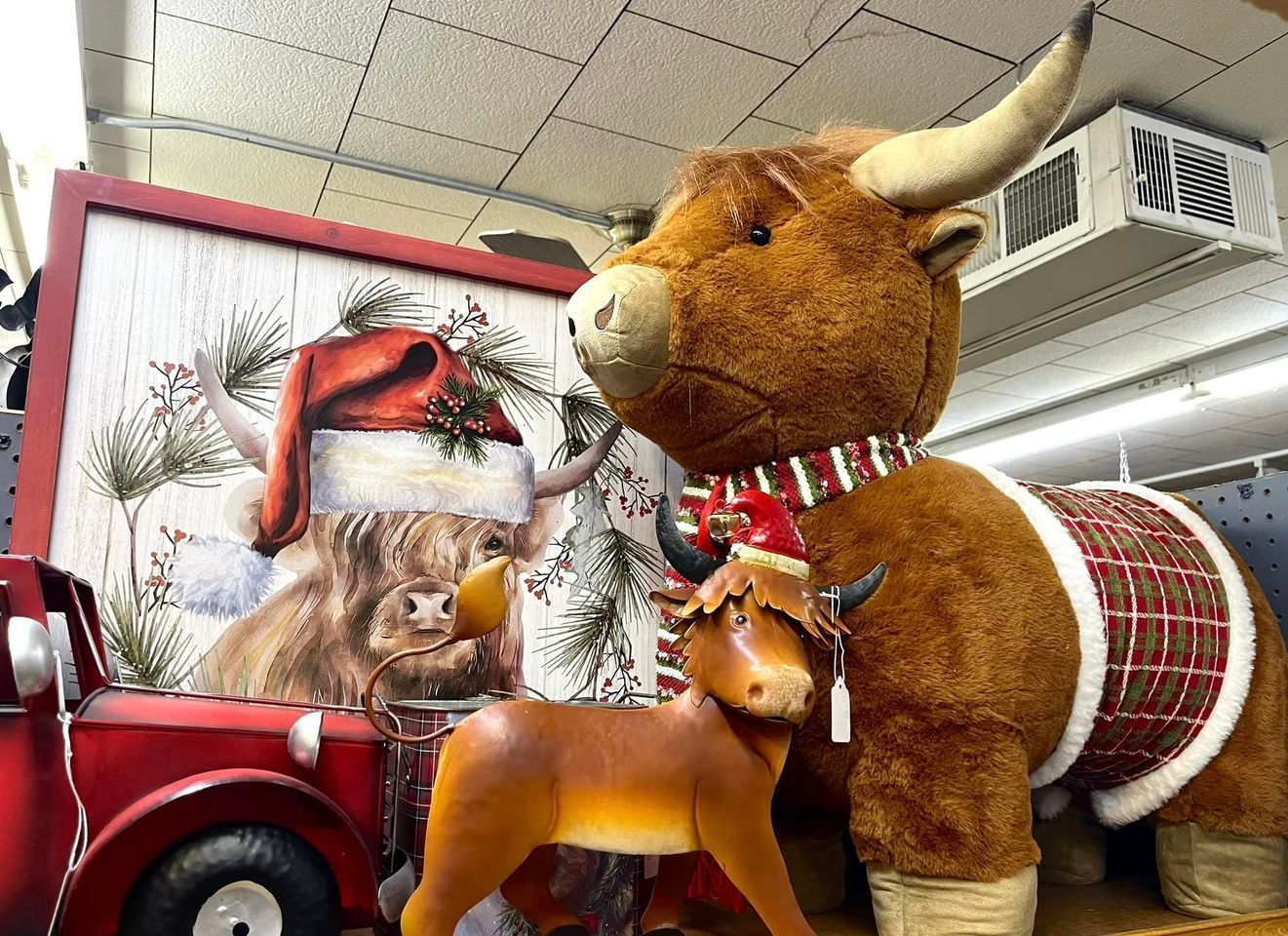 A display featuring a plush Highland cow in a holiday sweater, a small reindeer figure, and a festive red truck painting.