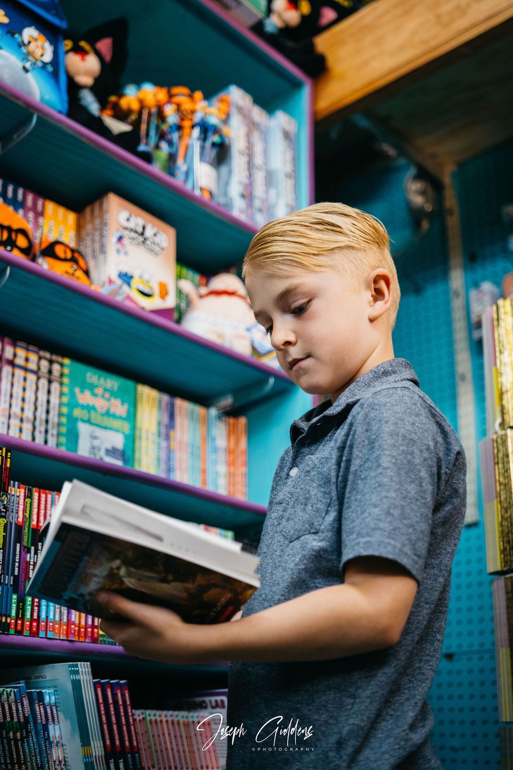 A person stands in a colorful bookstore, holding and reading a book in front of shelves stocked with books and merchandise.