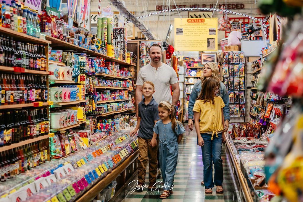 A family walks through the aisle of a store filled with shelves of various products.