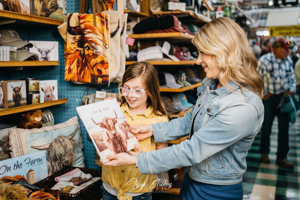 A person and a child look at a framed picture of a Highland cow in a shop filled with animal-themed gifts.