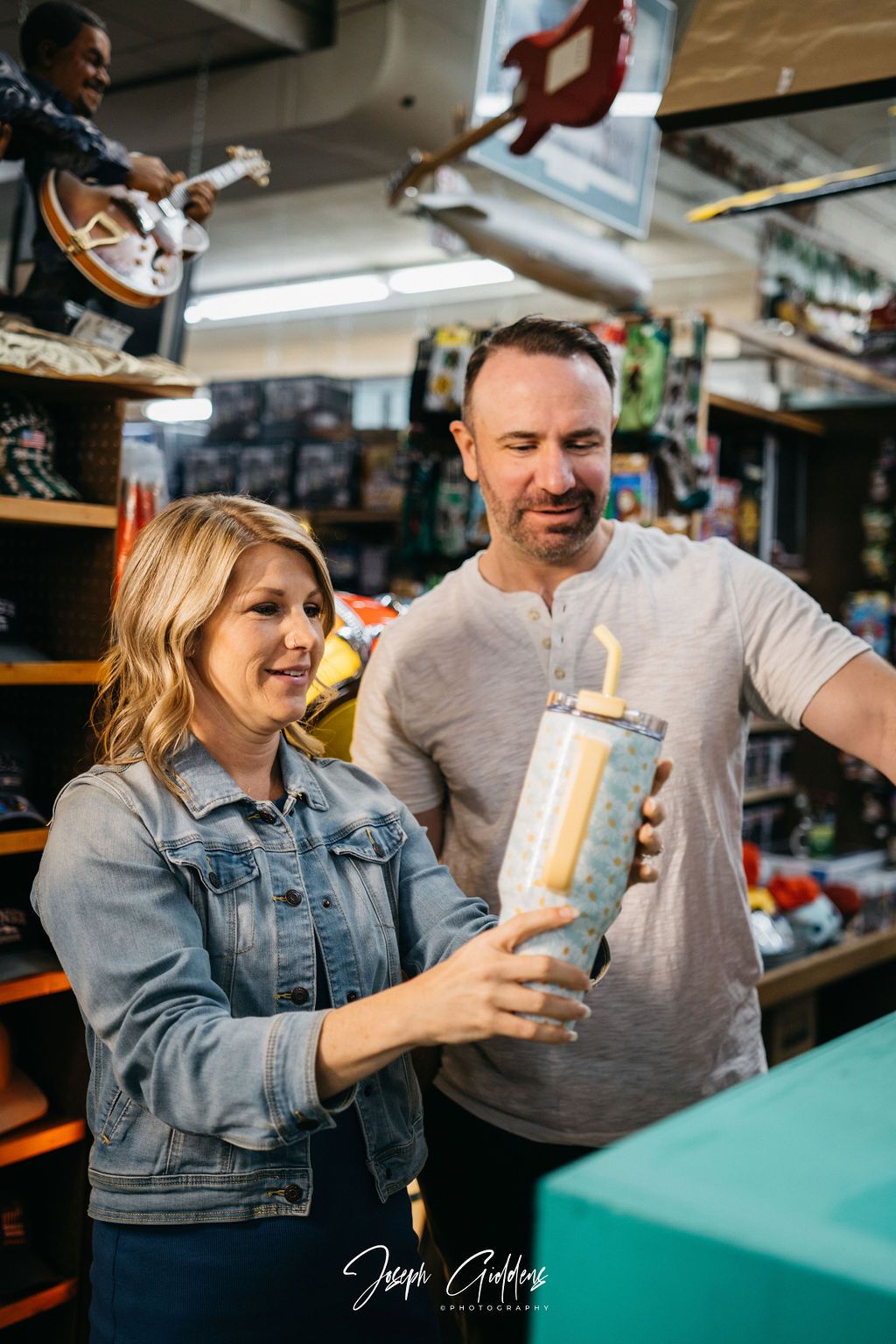 A woman and a man examine a light-colored tumbler with a straw while standing in a store filled with merchandise.