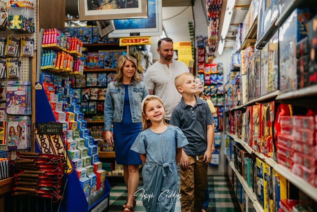 A family of four walks down the aisle of a toy store filled with shelves of games and merchandise.