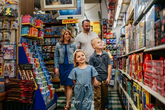 A family of four walks down the aisle of a toy store filled with shelves of games and merchandise.