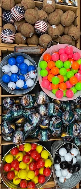 A wooden display rack filled with various types of sports balls in bins, including patterned, neon, and colored golf balls.