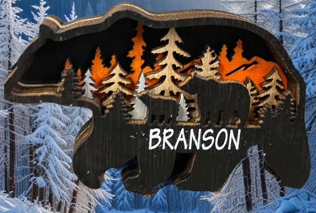 A layered wooden cutout of a bear silhouette featuring a forest scene and the word 