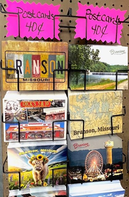 A display rack holding various Branson, Missouri postcards, with pink signs at the top listing the price at 40 cents each.