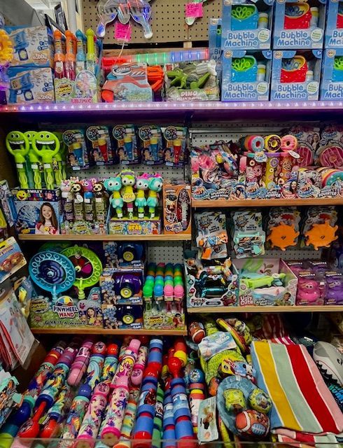 Shelves in a store filled with various colorful children's toys, including bubble wands, water guns, and plush items.
