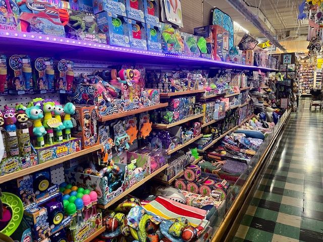 Shelves filled with various colorful toys and retail merchandise in a store aisle with purple accent lighting.