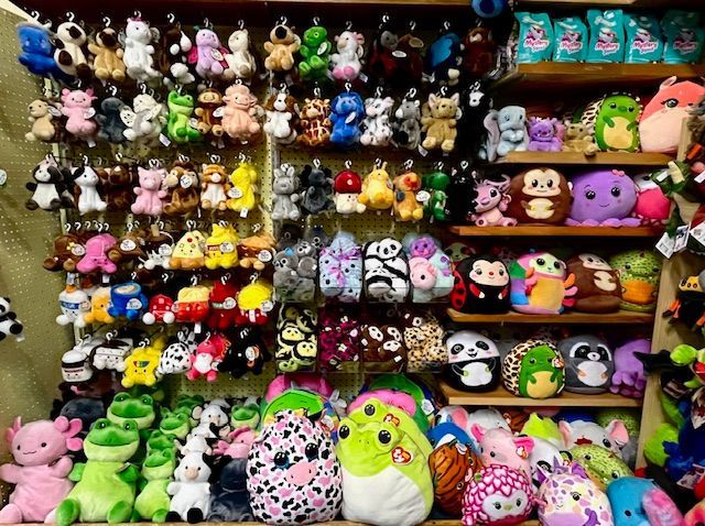 A retail display wall packed with various colorful plush toys and stuffed animals on hooks and wooden shelves.
