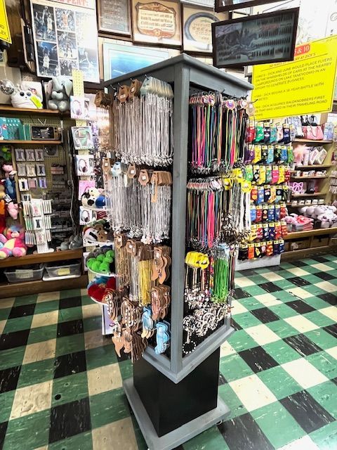A revolving display stand stocked with various necklaces and small retail items inside a gift shop with checkered floors.