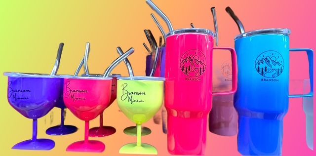 A variety of colorful tumblers and goblets with metal straws arranged against a vibrant gradient background.