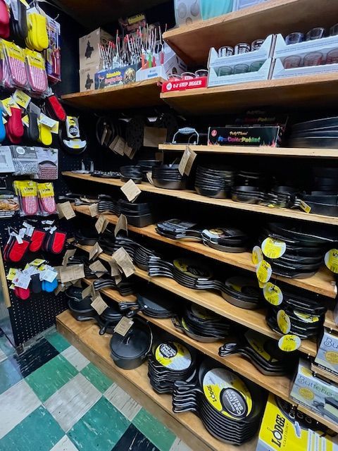 Shelves filled with various cast-iron skillets and colorful oven mitts in a retail store with green and white tiled floors.