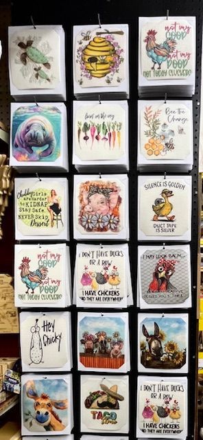 Vertical display rack showing 15 decorative towels with various whimsical animal, vegetable, and humor-themed illustrations.