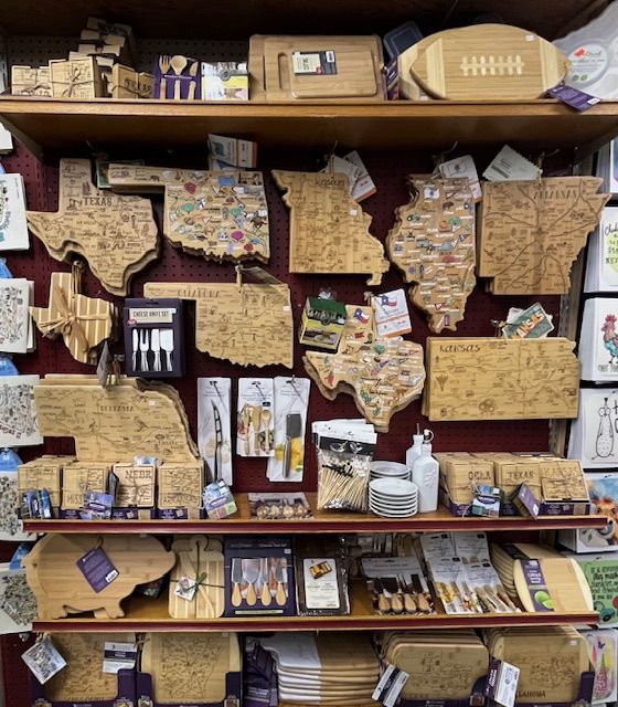 Display shelf filled with wooden state-shaped cutting boards, souvenir items, and small kitchen utensil sets.