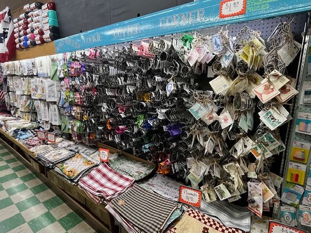 Retail display of assorted metal cookie cutters hanging on hooks above stacks of folded kitchen towels and linens.