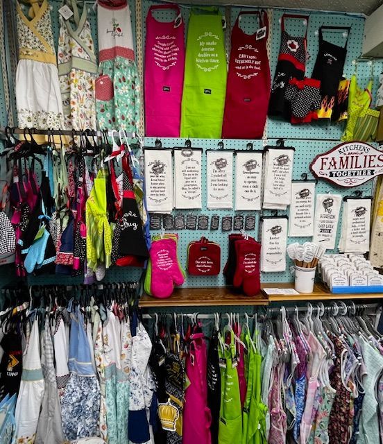 Display of colorful aprons, kitchen towels, and oven mitts arranged on a pegboard wall and racks in a retail shop.