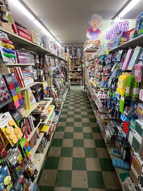 An aisle in a retail store with shelves stocked with various household goods and a green and white checkered floor.