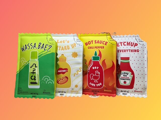 Four condiment packets arranged in a row: green wasabi, yellow mustard, red hot sauce, and red ketchup.